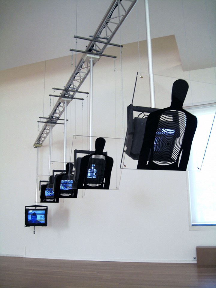 Dara Birnbaum
Hostage, 1994/2010
Installation - 6 channel color video with 6 channels of stereo audio; 4 plexiglass target/shields; inter-active last component, Approximately 36 feet long; plexiglass pantels each 2' x 2' x 3/4"
